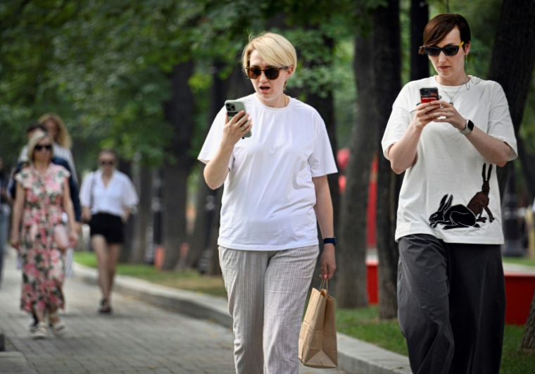 Des femmes utilisent leurs smartphones dans un parc à Moscou, le 30 juillet 2025 ( AFP / Alexander NEMENOV )