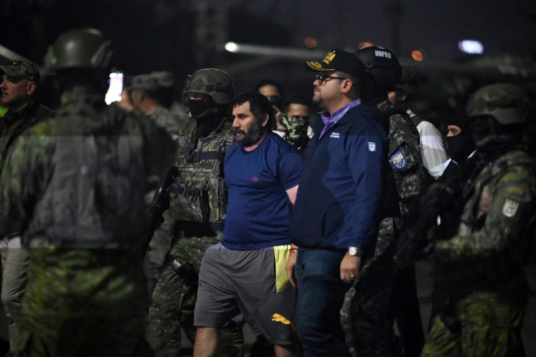 Le trafiquant de drogue Adolfo Macias (c), alias Fito, gardé par le ministre de l'Intérieur équatorien John Reimberg (2e d) et du personnel militaire à son arrivée à la base aérienne de Guayaquil, après sa recapture, le 25 juin 2025 à Manta, dans la province de Manabi, en Équateur ( AFP / MARCOS PIN )