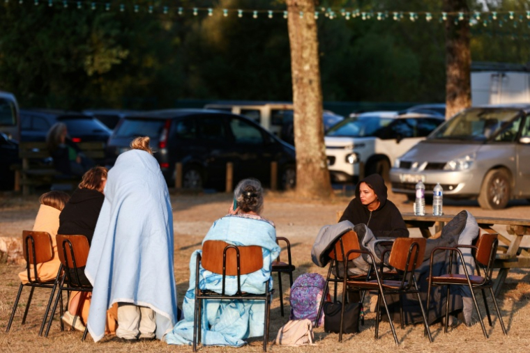 Des personnes, sac de couchage sur le dos,  sont assises devant une salle du Porge, en Gironde, après les évacuations décidées en raison de l'incendie qui sévit au nord du bassin d'Arcachon, le 23 juillet 2026 ( AFP / ROMAIN PERROCHEAU )
