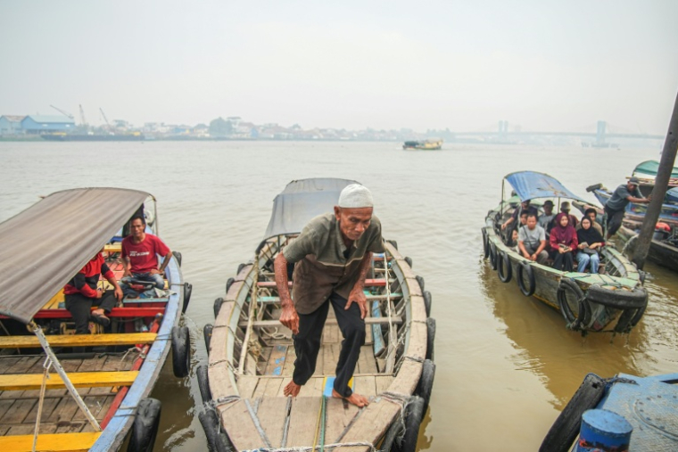 Des bateaux de passagers attendent de traverser la rivière Musi à Palembang, dans le sud de Sumatra, dans un épais brouillard causé par les fumées d'incendies, le 22 septembre 2026 ( AFP / AL ZULKIFLI )