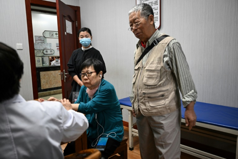 Meng Jia (au fond), une accompagnatrice de patient, assiste Gao Yingmin (c) et Tian Yigui (d) pendant une consultation avec un médeciin (g) dans un hôpital à Pékin, le 22 mai 2025 en Chine ( AFP / Jade GAO )