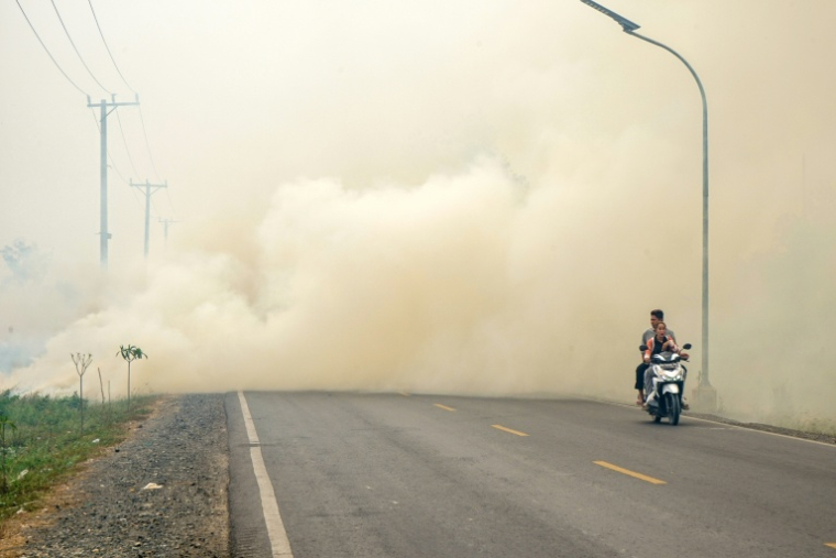 Un couple circule à moto à travers une épaisse fumée causée par des feux de forêt et de végétation dans la province de Kalimantan du Sud, à Bornéo, le 10 octobre 2026 ( AFP / MUDA SAGALA )