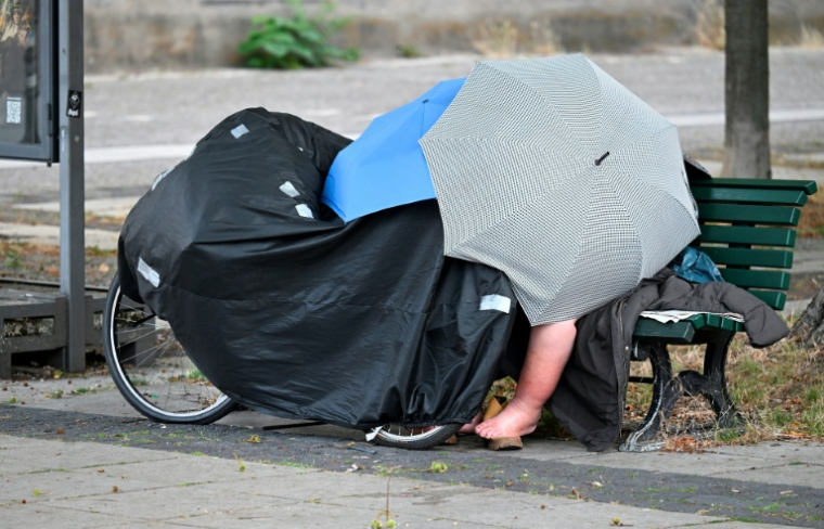 Un Sdf sur un banc public abrité sous des parapluies à Berlin le 28 juin 2026 ( AFP / RALF HIRSCHBERGER )