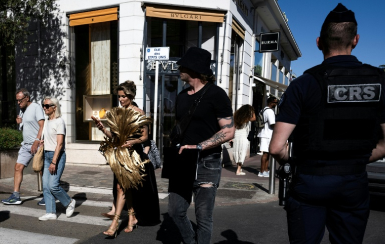 Une femme en tenue de soirée passe à côté d'un CRS en marge de la 79e édition du Festival de Cannes, le 12 mai 2026 ( AFP / Anna KURTH )