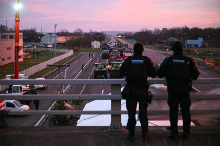 Des gendarmes observent les agriculteurs sur l'autoroute A64 lors d'un blocage pour protester contre l'abattage obligatoire des troupeaux de bovins atteints de dermatose nodulaire contagieuse et l'accord  UE-Mercosur, à Carbonne, le 13 janvier 2026 en Haute-Garonne ( AFP / Lionel BONAVENTURE )