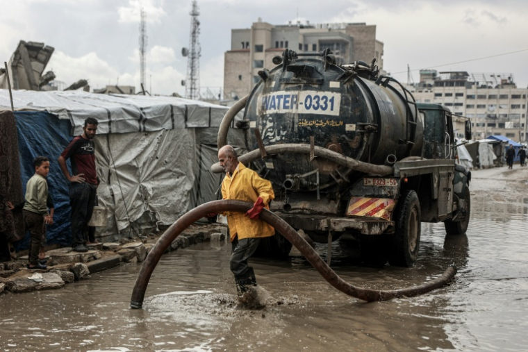 Un Palestinien nettoie l'eau stagnante sur la route près d'un camp de déplacés après les premières pluies hivernales à Gaza, le 14 novembre 2025 ( AFP / Omar AL-QATTAA )