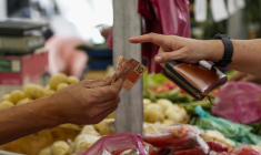 Un client paie en espèces à un étal de légumes sur un marché de rue à São Paulo (Brésil), le 25 août 2022. ( AFP / MIGUEL SCHINCARIOL )