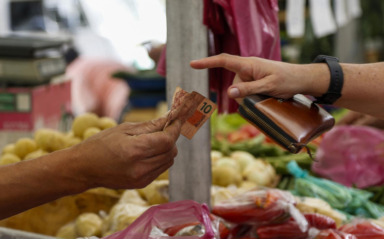 Un client paie en espèces à un étal de légumes sur un marché de rue à São Paulo (Brésil), le 25 août 2022. ( AFP / MIGUEL SCHINCARIOL )