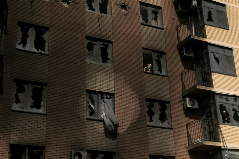 Un homme à travers une vitre brisée à l'intérieur d'un immeuble résidentiel endommagé par des frappes russes, à Kiev en Ukraine le 14 mai 2026 ( AFP / Roman PILIPEY )