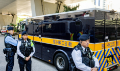 Des policiers surveillent un fourgon des services pénitentiaires transportant l'ex-magnat des médias Jimmy Lai à sa sortie du tribunal de West Kowloon après l'énoncé du verdict dans son procès pour atteinte à la sécurité nationale à Hong Kong, le 15 décembre 2025 ( AFP / Leung Man Hei )