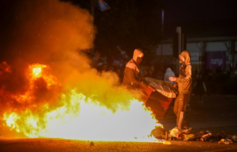 Des manifestants masqués alimentent un feu sur une route lors d'une troisième nuit d'émeutes visant des immigrés à Ballymena, en Irlande du Nord, le 11 juin 2025 ( AFP / PAUL FAITH )