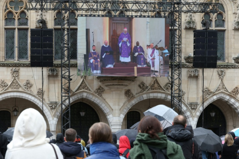 Des habitants assistent à la cérémonie d'obsèques du professeur de français Dominique Bernard, retransmise sur un écran géant installé sur la façade de l'hôtel de ville d'Arras, le 19 octobre 2023 dans le Pas-de-Calais ( AFP / Denis Charlet )