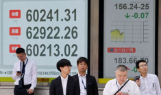 Des piétons passent devant un tableau de cotation boursière indiquant la moyenne des actions Nikkei à l'extérieur d'une maison de courtage à Tokyo