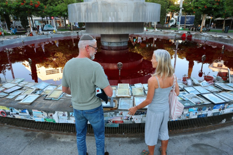 Des personnes se tiennent près de la fontaine Dizengoff, remplie de colorant rouge, dans la ville côtière israélienne de Tel-Aviv, pour marquer le troisième anniversaire de l'attaque du Hamas du 7 octobre, le 7 octobre 2026 ( AFP / Jack GUEZ )