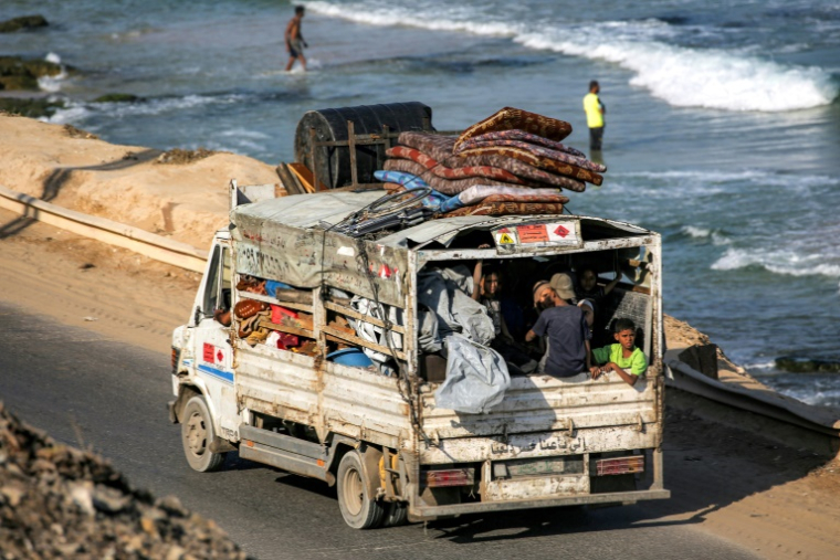 Des déplacés palestiniens fuyant le nord de la bande de Gza en direction du sud du terrtoire roulent à bord d'un camion chargé d'effets personnels sur la route côtière du camp de Nousseirat (centre), le 30 août 2025 ( AFP / Eyad BABA )