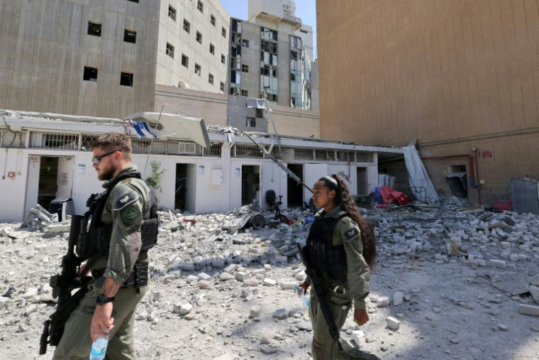Des soldats israéliens patrouillent devant des bâtiments de l'hôpital Soroka de Beersheva, dans le sud d'Israël, touché par une frappe iranienne le 19 juin 2025 ( POOL / Marc Israel SELLEM )