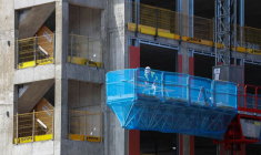 Un ouvrier du bâtiment effectue des travaux depuis une nacelle élévatrice montée sur mât, sur le chantier du complexe immobilier « Hatters Yard » à Stockport