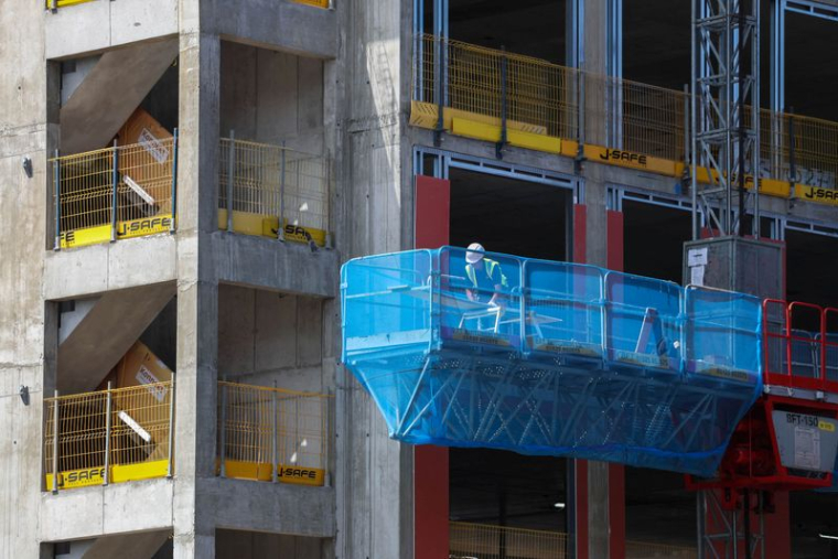 Un ouvrier du bâtiment effectue des travaux depuis une nacelle élévatrice montée sur mât, sur le chantier du complexe immobilier « Hatters Yard » à Stockport