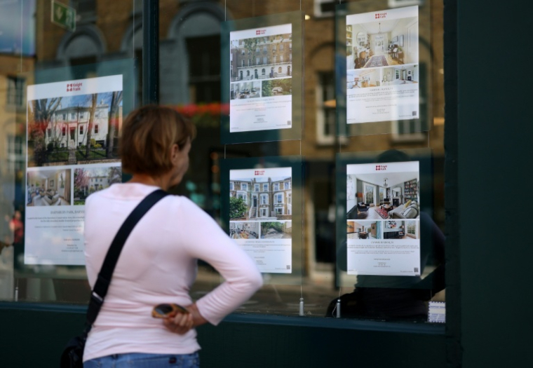 Une passante regarde les annonces immobilières à l'entrée d'une agence à Londres le 18 juin 2026 ( AFP / Toby Shepheard )