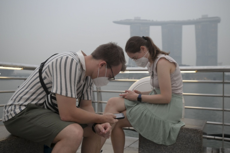 Des touristes portent des masques de protection contre les fumées générées par les incendies indonésiens, le 15 octobre 2026 à Singapour ( AFP / FELINE LIM )
