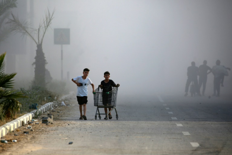De la fumée lors d'une frappe israélienne alors que des Palestiniens marchent sur une route utilisée pour atteindre un point de distribution d'aide de la Fondation humanitaire de Gaza (GHF,) près du camp de réfugiés de Nousseirat, dans le centre de la bande de Gaza, le 25 juin 2025 ( AFP / Eyad BABA )