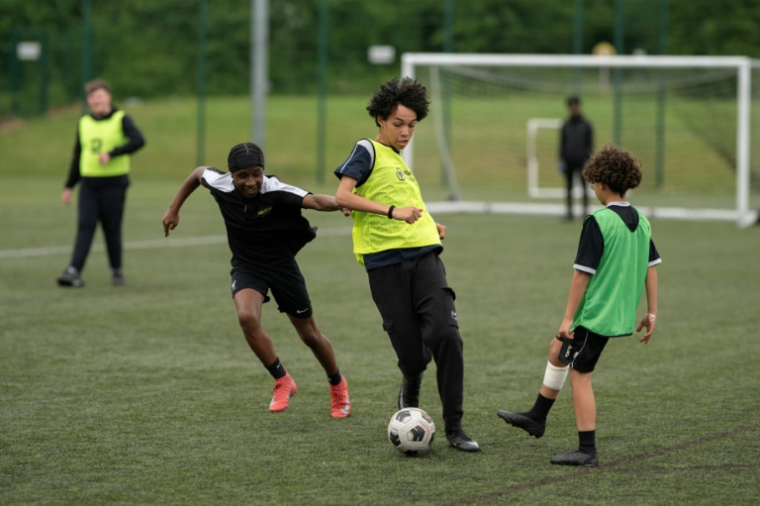 Fabian Myers (c) et Kaziah Cameron (2e g), élèves du collège-lycée publicOur Lady and St Chad Catholic Academy et participants du programme "Football Beyond Borders" (FBB), disputent un match de foot avec d'autres élèves du programme à Wolverhampton, le 12 juin 2026 au Royaume-Uni ( AFP / Oli SCARFF )