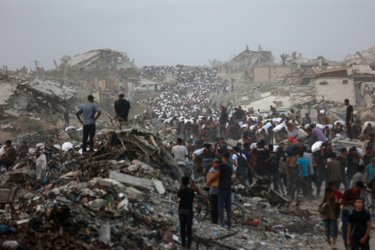 Des Palestiniens, au milieu des décombres sur le chemin côtier de Beit Lahia, dans la bande de Gaza, transportent l'aide alimentaire qu'ils ont pu se procurer le 29 juillet 2025 ( AFP / Omar AL-QATTAA )