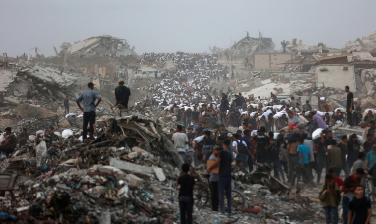 Des Palestiniens, au milieu des décombres sur le chemin côtier de Beit Lahia, dans la bande de Gaza, transportent l'aide alimentaire qu'ils ont pu se procurer le 29 juillet 2025 ( AFP / Omar AL-QATTAA )
