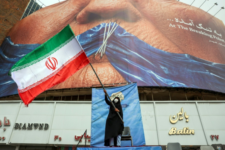 Une femme agite un drapeau iranien devant un panneau anti-américain en référence à Donald Trump et à la fermeture du détroit d'Ormuz, le 5 mai 2026 à Téhéran ( AFP / - )