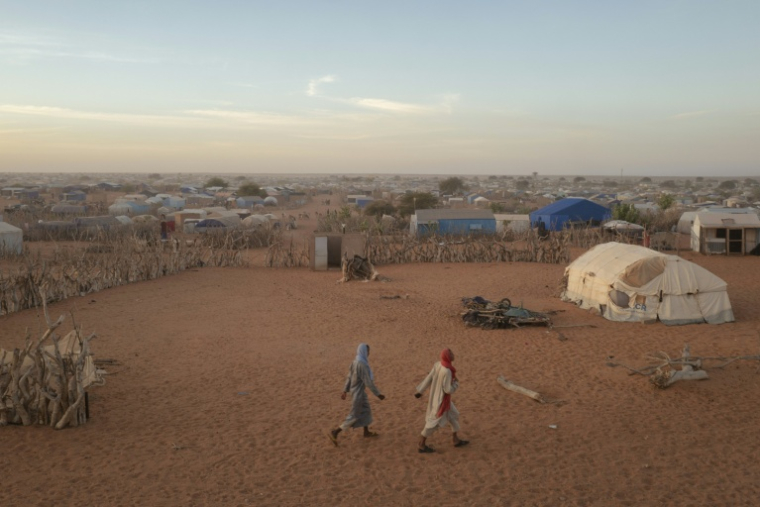 Deux hommes passent devant des abris et des tentes dans le camp de réfugiés de M’berra, situé dans le sud-est de la Mauritanie, qui accueille 120 090 réfugiés ayant fui les violences et l’instabilité au Mali, à Bassikonou, le 3 novembre 2025. ( AFP / MICHELE CATTANI )