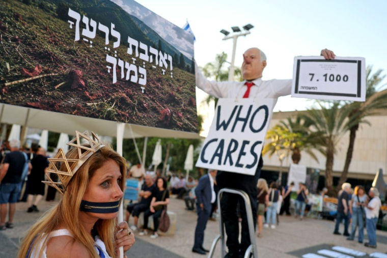 Une manifestante aux côtés d'un homme portant un masque à l'effigie du Premier ministre israélien Benjamin Netanyahu lors d'un rassemblement contre le gouvernement et la guerre à Gaza, le 2 juillet 2026 sur la "Place des Otages" à Tel-Aviv, marquant le millième jour depuis l'attaque du Hamas contre Israël le 7 octobre 2023 ( AFP / Jack GUEZ )