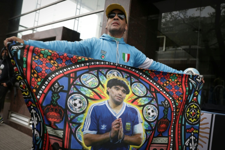 Un supporter tient un drapeau à l'effigie de Diego Maradona, avant une audience du procès sur le décès de la légende du football argentin, devant le tribunal à San Isidro, le 8 octobre 2026 en Argentine ( AFP / STRINGER )