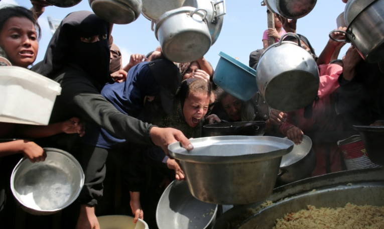 Des femmes et des enfants palestiniens tendent leurs casseroles vides devant une cuisine communautaire à Khan Younes, dans le sud de la bande de Gaza, le 21 août 2025 ( AFP / - )