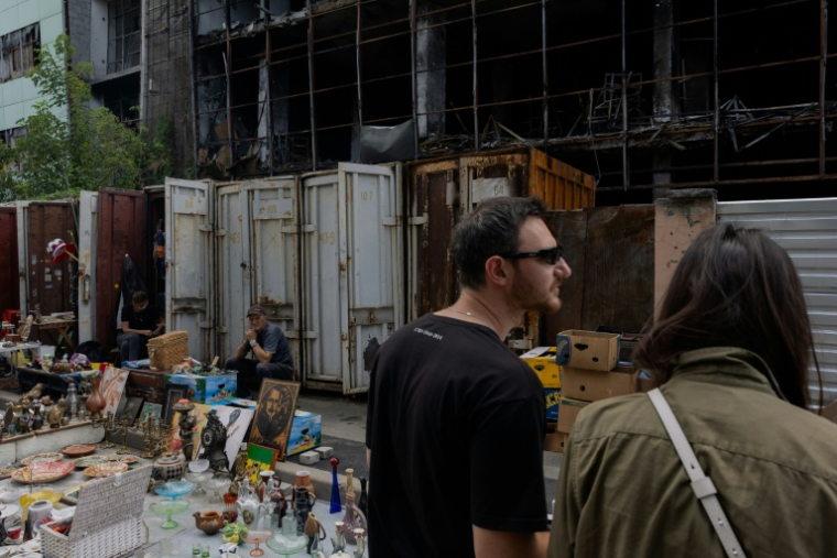 Des vendeurs du marché aux puces de Potchaïna endommagé par une frappe russe, à Kiev, le 9 août 2026 en Ukraine ( AFP / Tetiana DZHAFAROVA )