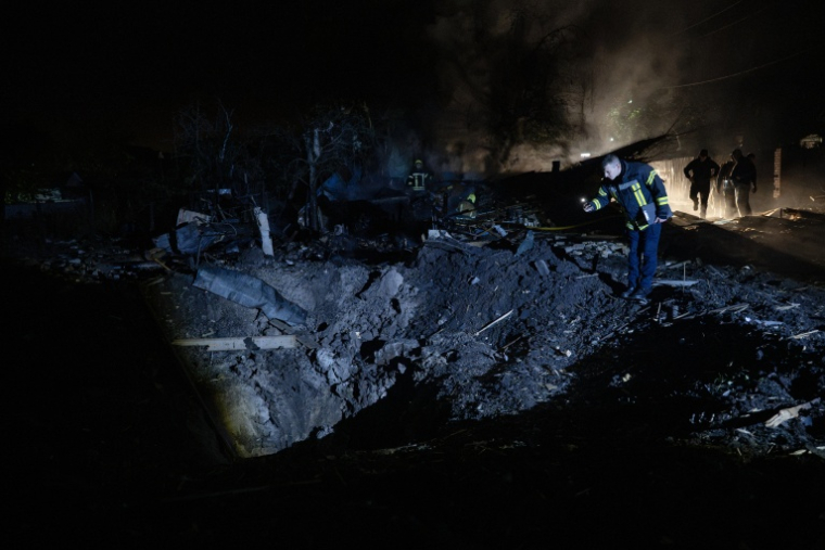 Un pompier ukrainien examine un cratère après une frappe de missile russe qui a touché des habitations à Kiev dans la soirée du 21 octobre 2026 ( AFP / Genya SAVILOV )