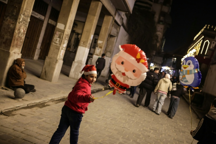Des enfants se promènent avec des ballons de Noël dans un quartier chrétien de Damas, le 22 décembre 2025 en Syrie ( AFP / Bakr ALkasem )