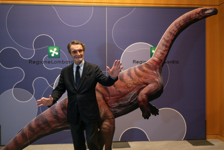Attilio Fontana, président de la région italienne de Lombardie, pose pour une photo avec un dinosaure en carton lors d'une conférence de presse pour présenter la découverte de milliers d'empreintes de dinosaures dans le parc national du Stelvio, en Italie, près des zones qui accueilleront les Jeux olympiques d'hiver e Milan-Cortina 2026, à Milan, le 16 décembre 2025. On estime que ces empreintes appartiennent à des dinosaures prosauropodes du Trias supérieur, datant de 210 millions d'années. ( AFP / Piero CRUCIATTI )