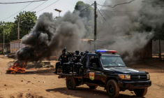 Un véhicule des forces de l'ordre passe à proximité  de pneus enflammés lors d'échauffourées dans la capitale bissau-guinéenne, le 29 novembre 2025 ( AFP / Patrick MEINHARDT )