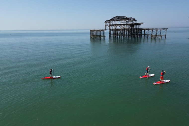 Des adeptes du paddleboard passent devant la jetée ouest abandonnée de Brighton, sur la côte sud de l'Angleterre, le 25 mai 2026, alors que la vague de chaleur s'étend à certaines régions du sud-est et à Londres ( AFP / Ben STANSALL )