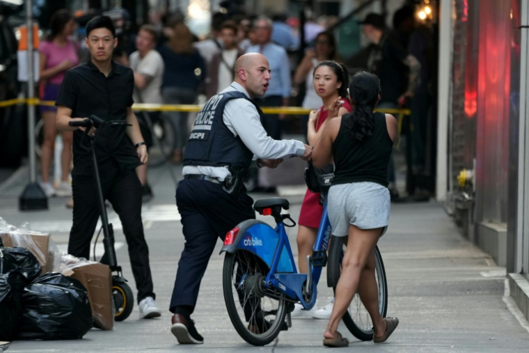 Un policier échange avec une cycliste sur le lieu de la fusillade à New York, le 28 juillet 2025 ( AFP / TIMOTHY A. CLARY )