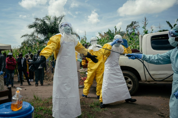 Des membres de la Croix-Rouge congolaise, en combinaison de protection, se désinfectent après avoir préparé le cercueil d'une femme soupçonnée d'être décédée de la maladie à virus Ebola, le 7 juin 2026 à Bunia, en RDC ( AFP / Jospin Mwisha )