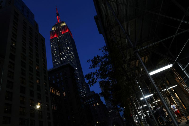 L'Empire State Building est illuminé en rouge alors que des personnes marchent dans le quartier de Midtown à New York