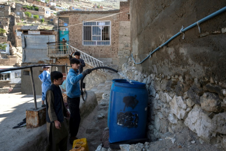 Des habitants remplissent des bidons d'eau potable à partir d'un camion-citerne sur les hauteurs de Kaboul, le 27 avril 2025 en Afghanistan ( AFP / Wakil KOHSAR )