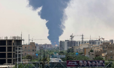 Des portraits de généraux et scientifiques iraniens tués par Israël sont affichés au-dessus d'une route à Téhéran, tandis qu'un panache de fumée épaisse et de feu s'élève d'un dépôt de carburant touché par une frappe, le 15 juin 2025 ( AFP / ATTA KENARE )