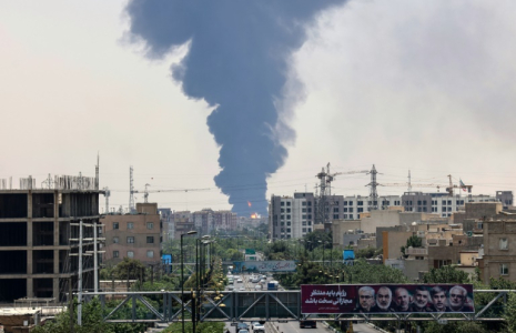 Des portraits de généraux et scientifiques iraniens tués par Israël sont affichés au-dessus d'une route à Téhéran, tandis qu'un panache de fumée épaisse et de feu s'élève d'un dépôt de carburant touché par une frappe, le 15 juin 2025 ( AFP / ATTA KENARE )