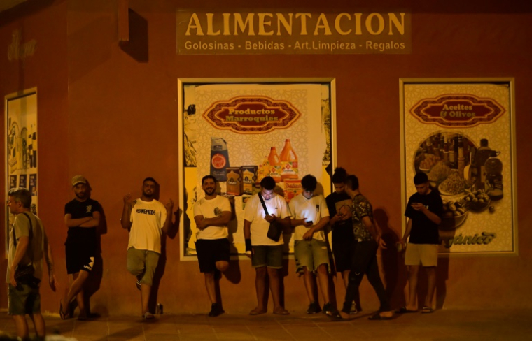 Des jeunes hommes consultent leurs téléphones portables à Torre Pacheco (Espagne), le 15 juillet 2025, alors qu'un rassemblement a été appelé par des groupes d'extrême droite après quatre jours de manifestations et de violences anti-migrants ( AFP / JOSE JORDAN )