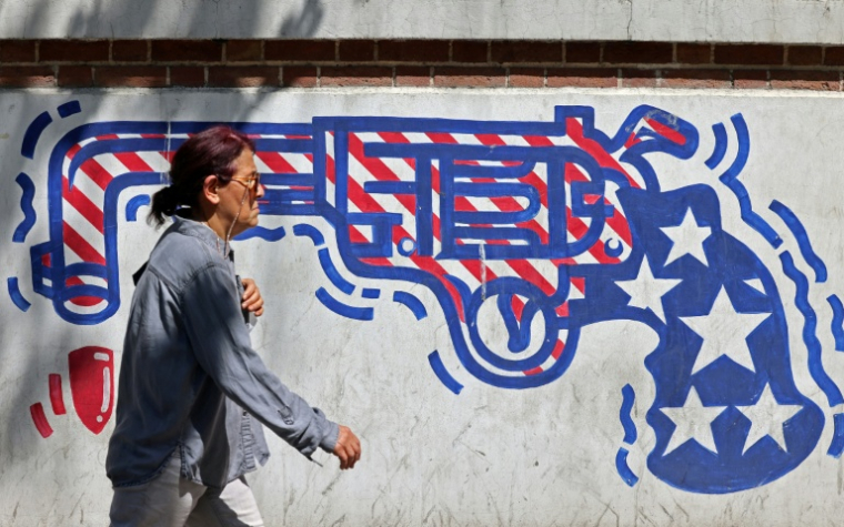 Un passante devant une fresque anti-américaine sur le mur de l'ancienne ambassade américaine à Téhéran, le 11 avril 2026 ( AFP / ATTA KENARE )