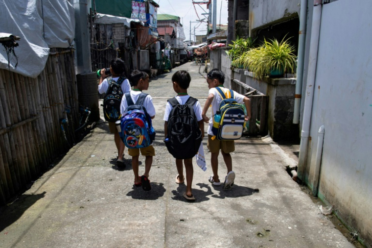 Des enfants sur un trottoir sec, en chemin pour l'école, sur l'île de Pugad, dans la province de Bulacan, le 7 juillet 2025 aux Philippines ( AFP / Ted ALJIBE )