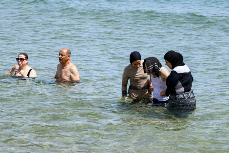 Des femmes aident une personne âgée à se baigner dans les eaux de la mer Méditerranée sur une plage de La Marsa, près de Tunis, le 14 juillet 2026 ( AFP / FETHI BELAID )