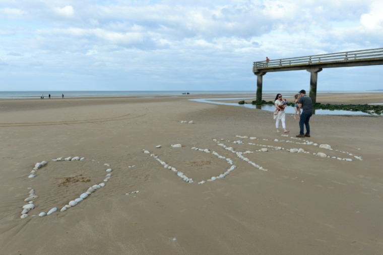 Une famille sur "Omaha Beach", où le mot "D-Day" a été tracé à l'aide de galets, à  Vierville-sur-Mer, dans le Calvados, lors des célébrations du 75e anniversaire du Débarquement en juin 2019 ( AFP / JEAN-FRANCOIS MONIER )